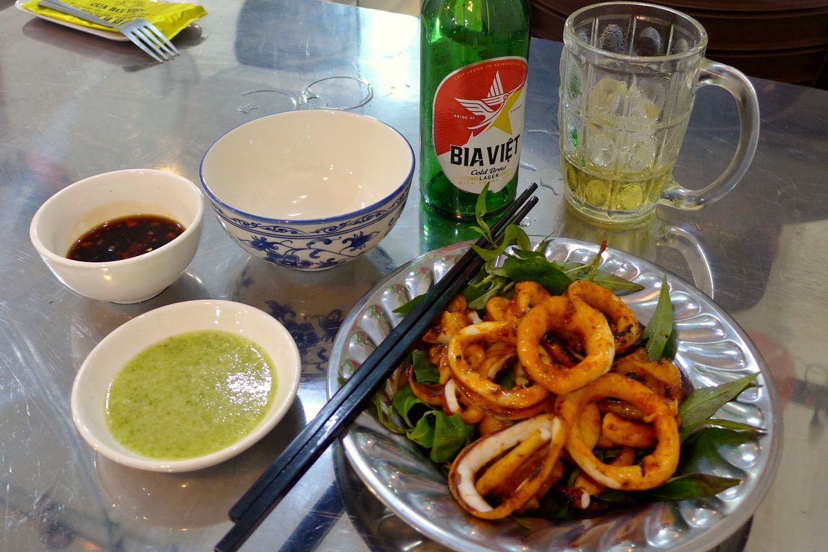 Đĩa mực chiên, chén nước chấm và chai bia trên bàn ăn